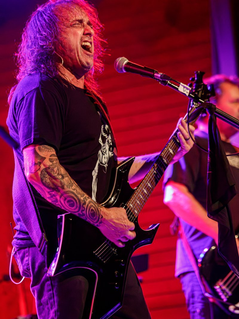 Rick Lemperes at the microphone mid-line, guitar slung low against a red backdrop