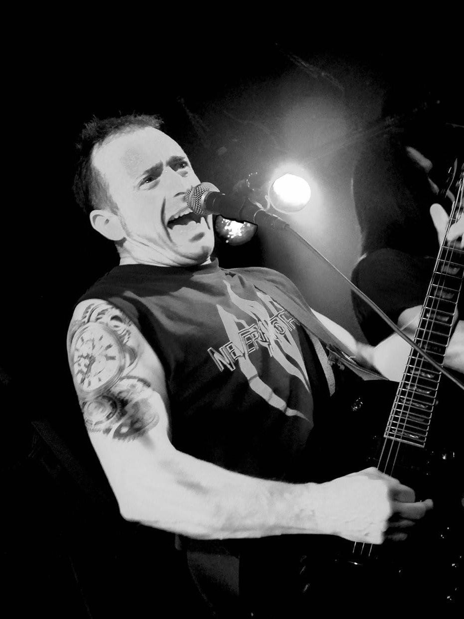 A vocalist caught mid-shout in black and white, a stage lamp flaring past the microphone